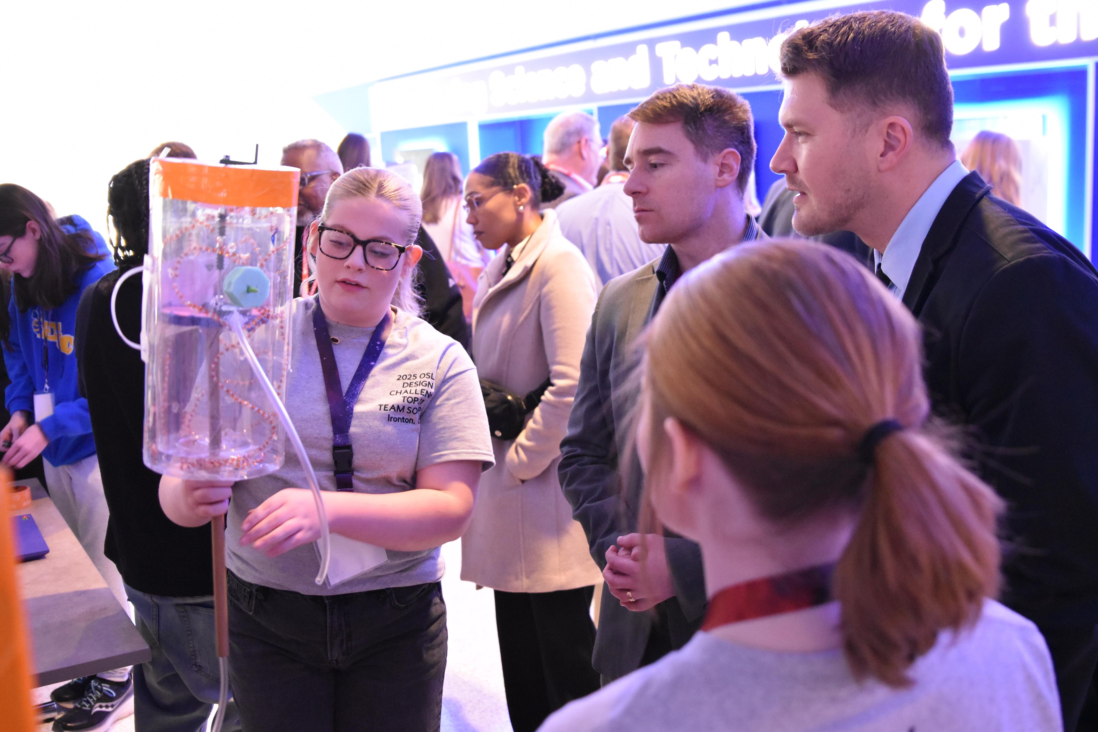 student showing a science project to two adults in a presentation